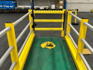 Industrial safety gate with yellow barriers and a floor warning sign reading "Watch Out" with a forklift icon.